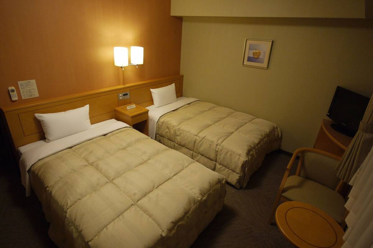 A hotel room with two beds, a nightstand, a television, and a chair.
