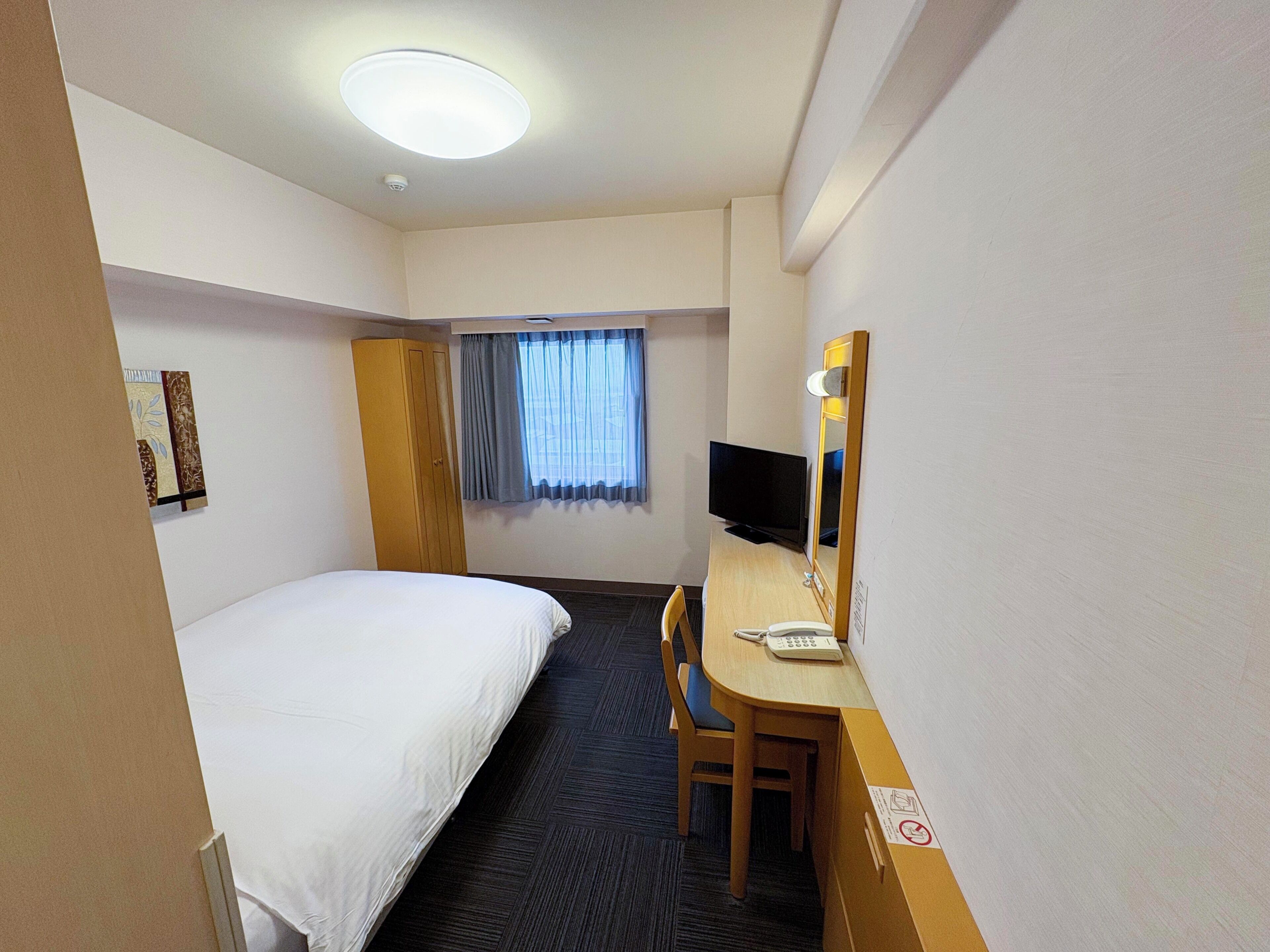 A hotel room with a bed, a desk with a computer, a chair, a television, and a window with curtains.