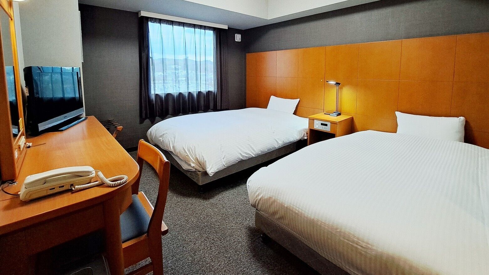 A hotel room with two beds, a desk with a telephone, a TV, and a lamp.