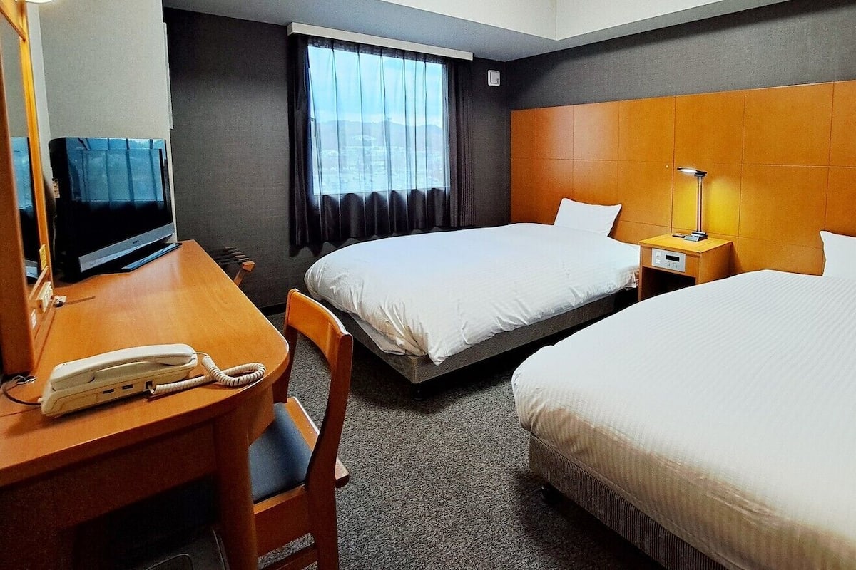 Une chambre d’hôtel avec deux lits, un bureau avec un téléphone, une télévision et une lampe.