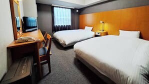 Habitación de hotel con dos camas, un escritorio con teléfono, una silla, un televisor y una ventana con cortinas.
