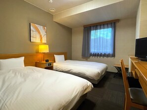 Een hotelkamer met twee bedden, een bureau met een televisie, een raam met gordijnen en een schilderij aan de muur.