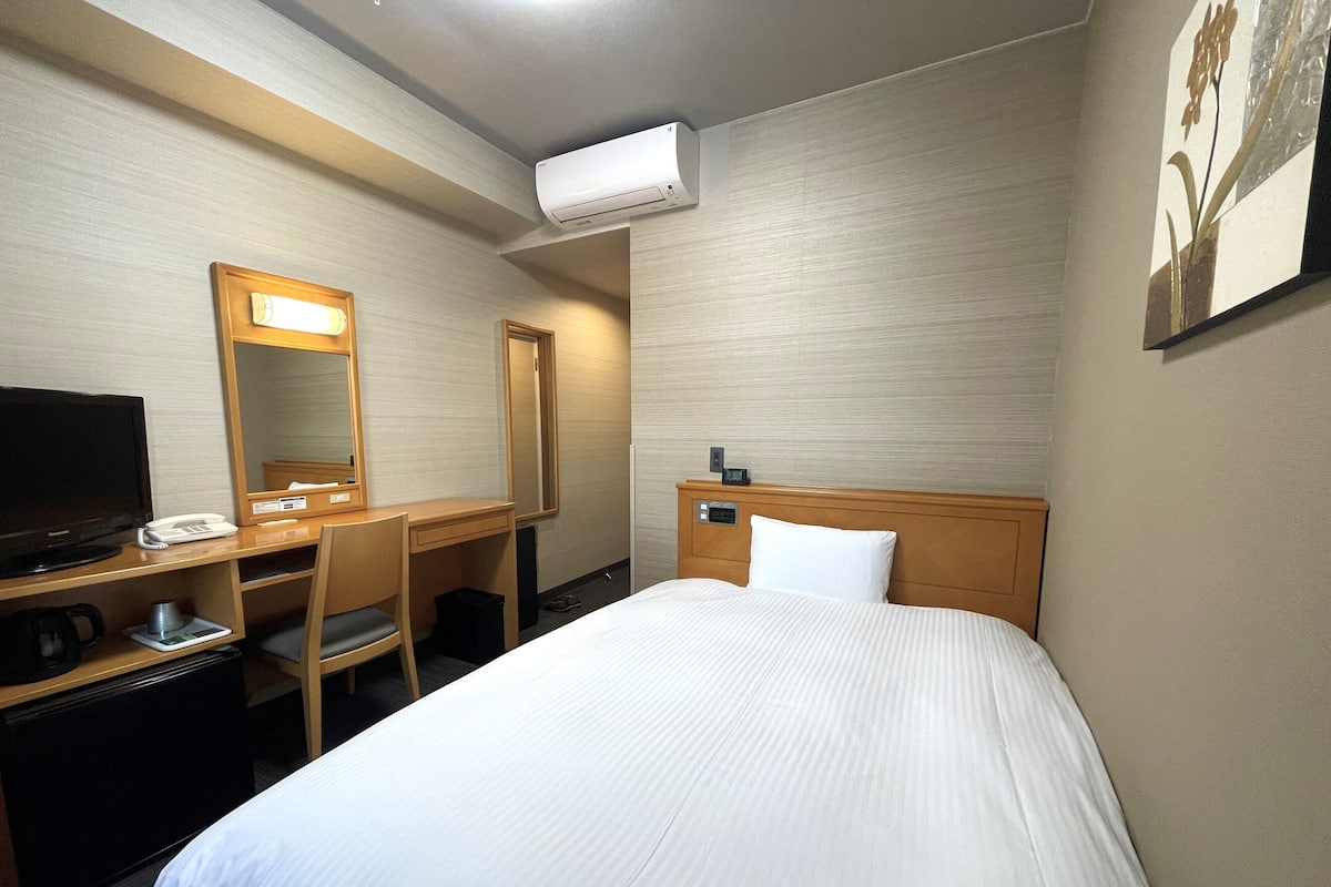 Une chambre d’hôtel équipée d’un lit, d’un bureau avec une chaise, d’une télévision, d’un téléphone et d’un appareil de climatisation.