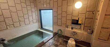 Un baño con pared de piedra, cabina de ducha con cristal, lavamanos y retrete.