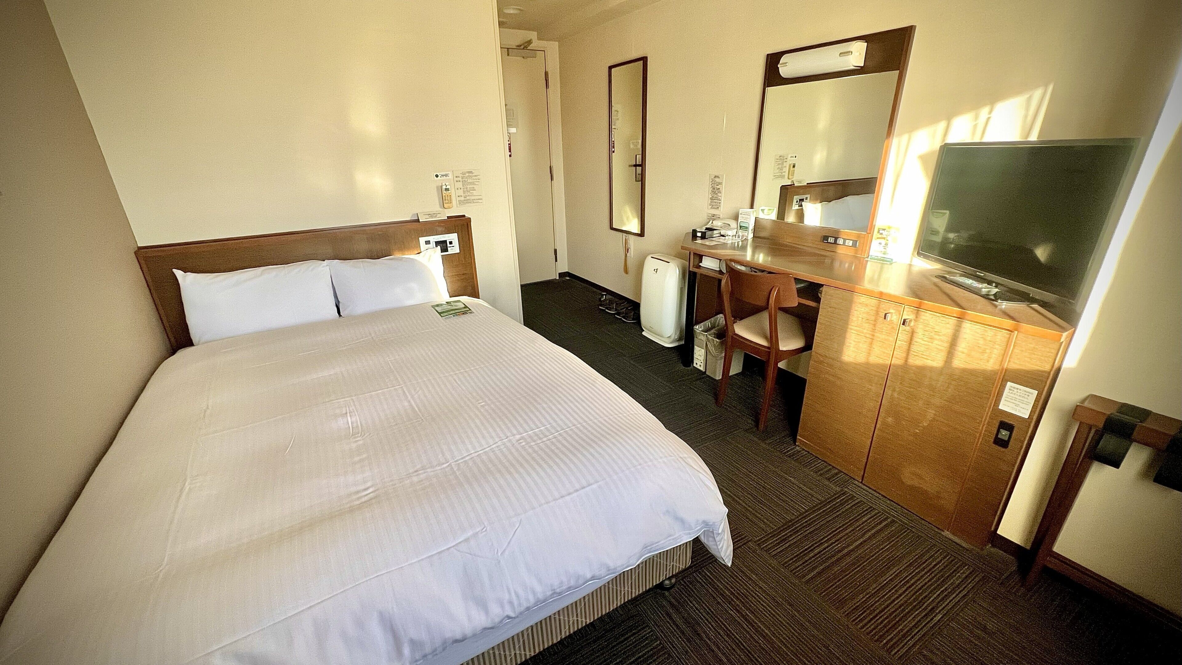 Una habitación de hotel con cama, escritorio, silla, televisor y espejo.