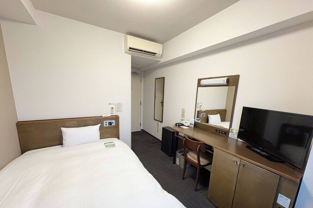 A hotel room with a large bed, a desk with a chair, a television, and a mirror.