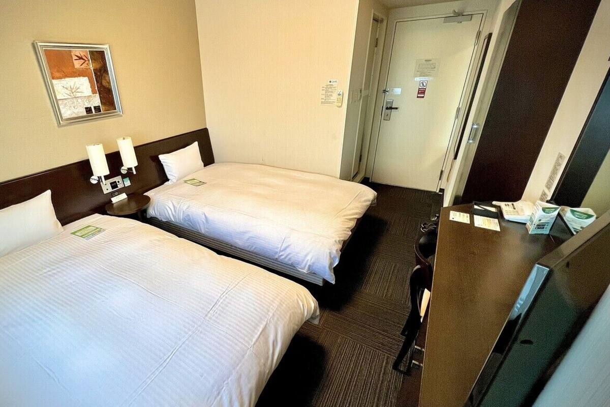 A hotel room with two beds, a nightstand, a wall-mounted lamp, and a door with a sign.