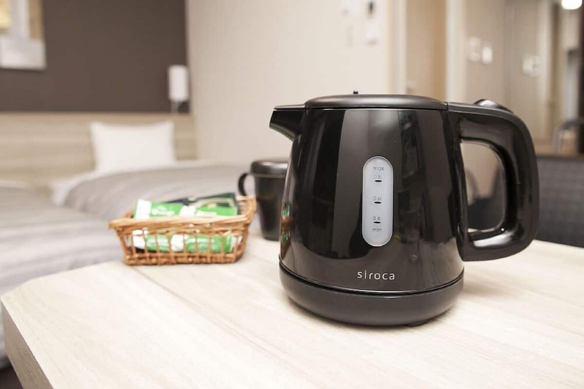 A black electric kettle on a wooden table with a basket of green items and a black mug in the background.