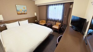 Una habitación de hotel con una cama grande, un escritorio con televisor, una silla y una mesita.