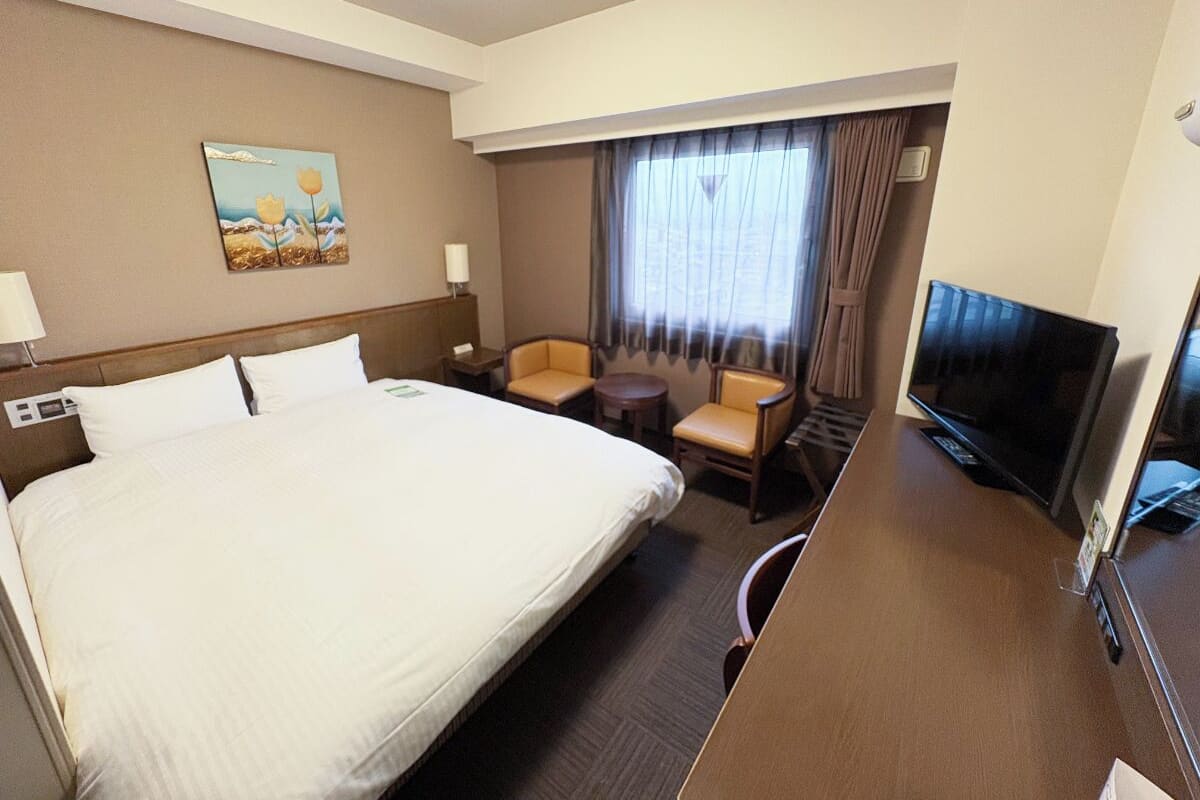 A hotel room with a large bed, a desk with a television, a chair, and a small table.