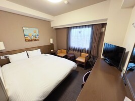 Una habitación de hotel con una cama grande, un escritorio con televisor, una silla y una mesita.