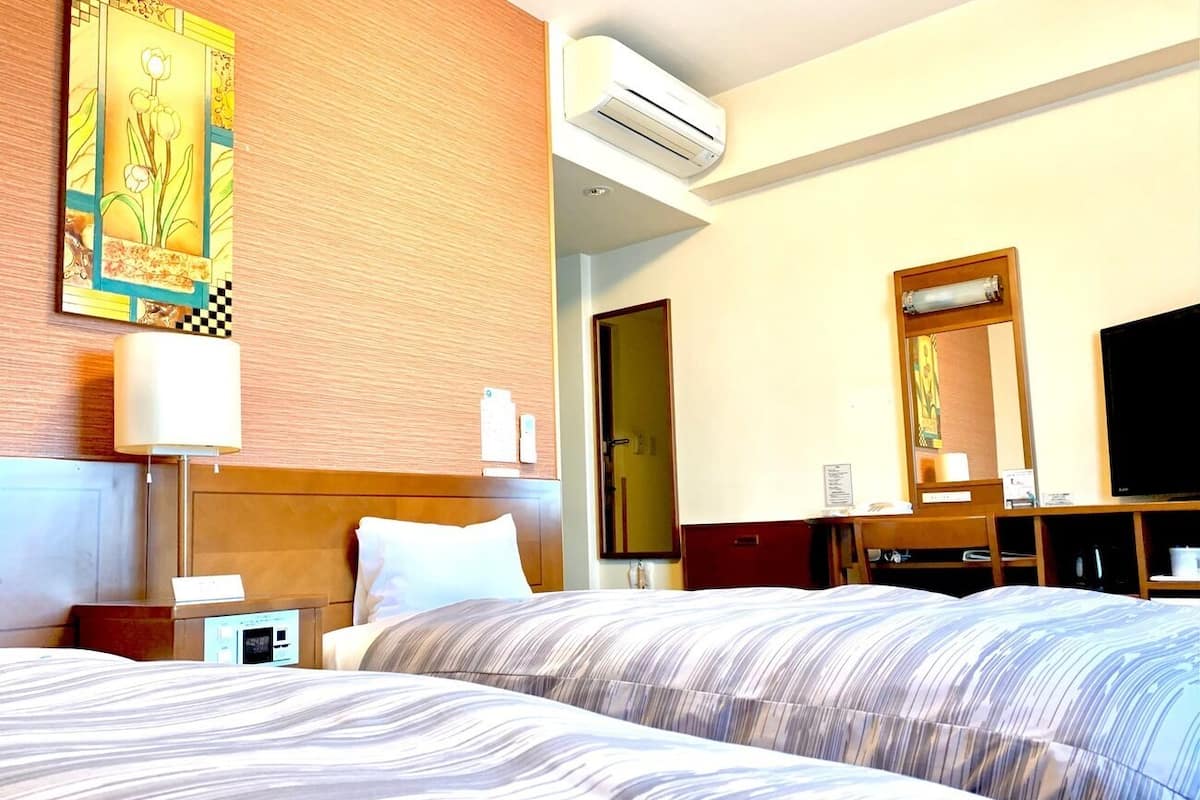 Quarto de hotel com cama, escrivaninha, ar condicionado, televisão e um quadro na parede.