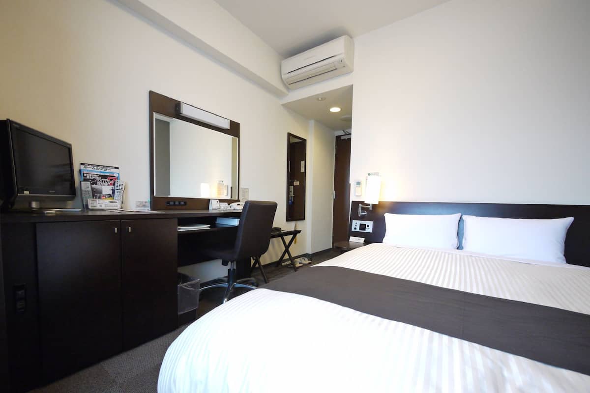 A hotel room with a large bed, a desk with a chair, a television, and a mirror.