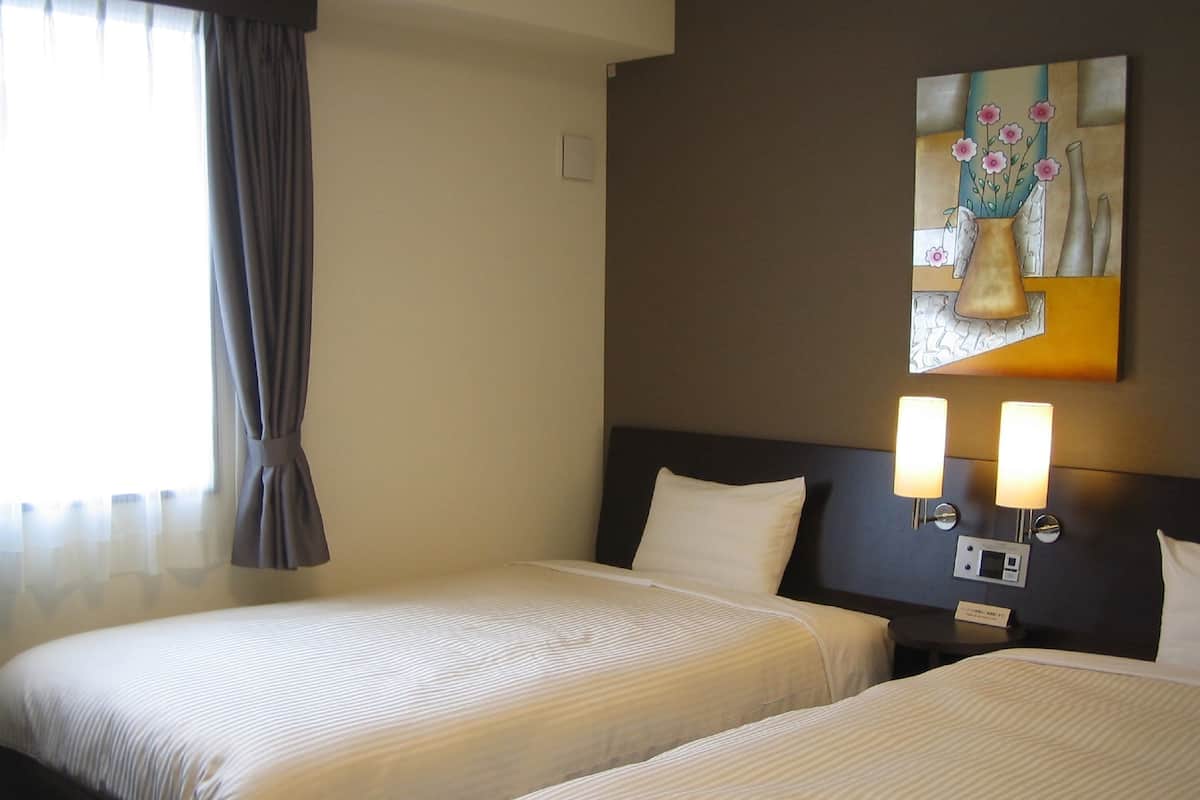 A hotel room with two beds, a painting on the wall, and a bedside table with lamps.