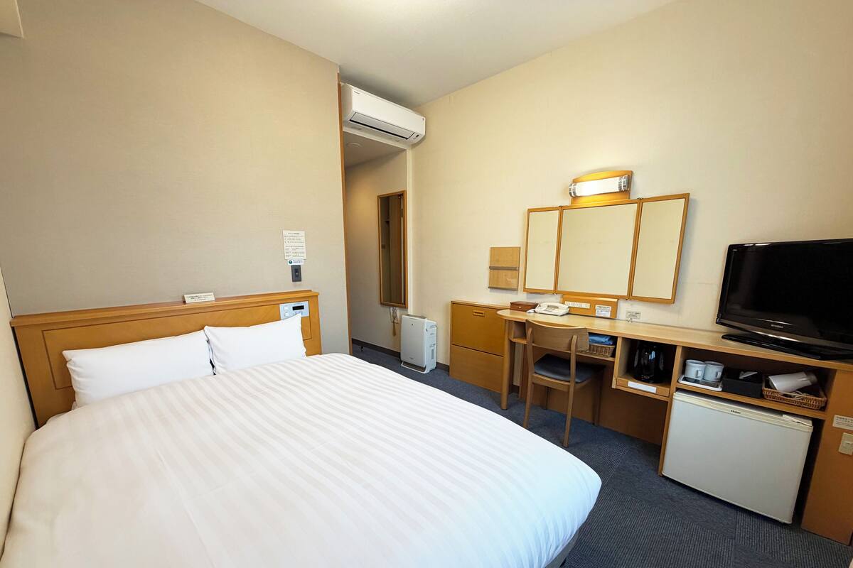Hotellihuone, jossa on sänky, työpöytä, tuoli, televisio ja pieni jääkaappi.
