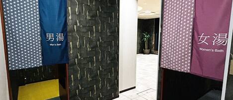 A hallway with a patterned wall, a potted plant, and directional signs.
