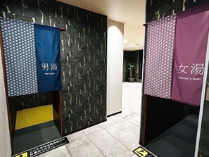 A hallway with a patterned wall, a potted plant, and directional signs.