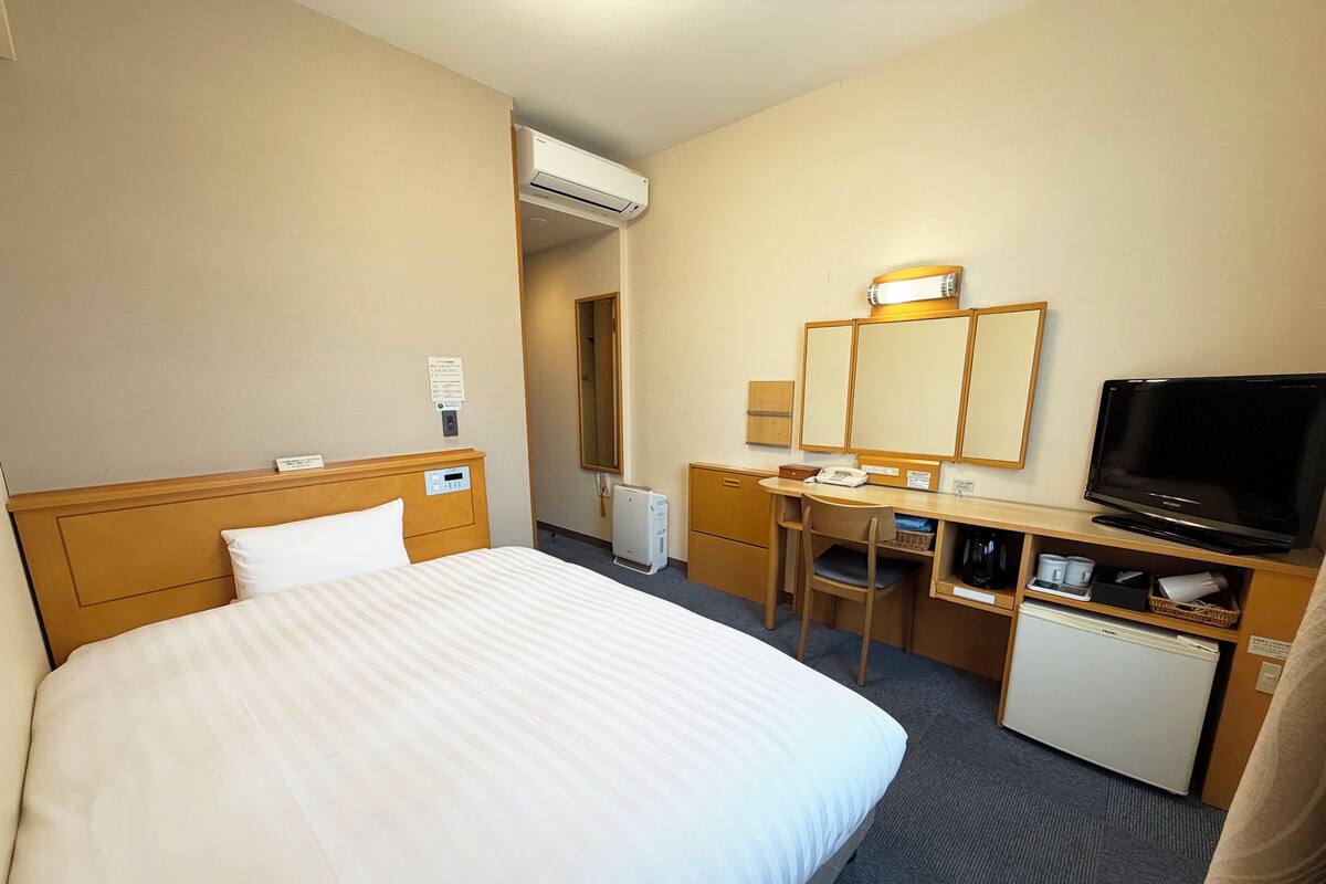 Hotellihuone, jossa on sänky, työpöytä, tuoli, televisio ja pieni jääkaappi.