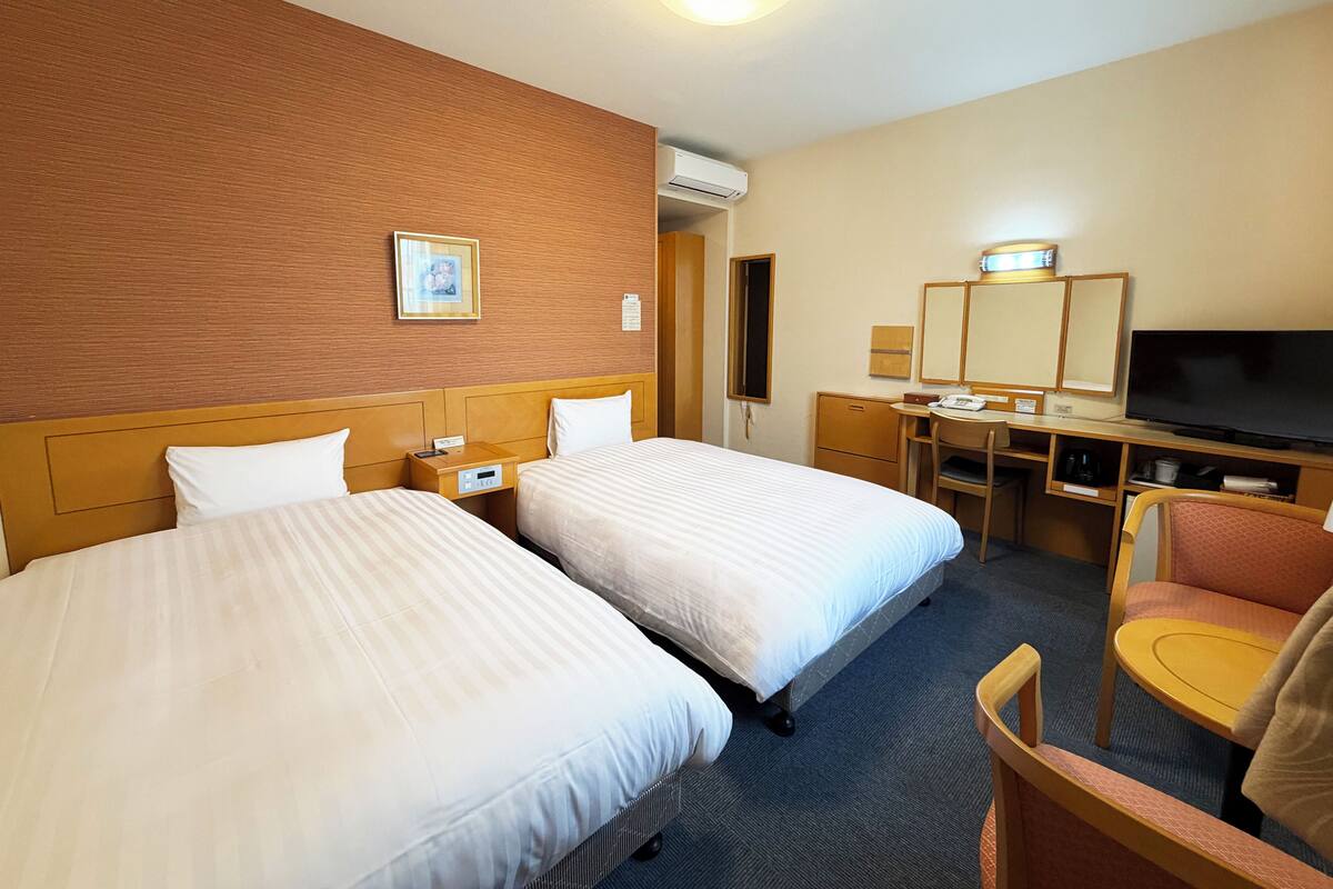 Hotellihuone, jossa on kaksi sänkyä, työpöytä tuolilla, televisio ja peili.