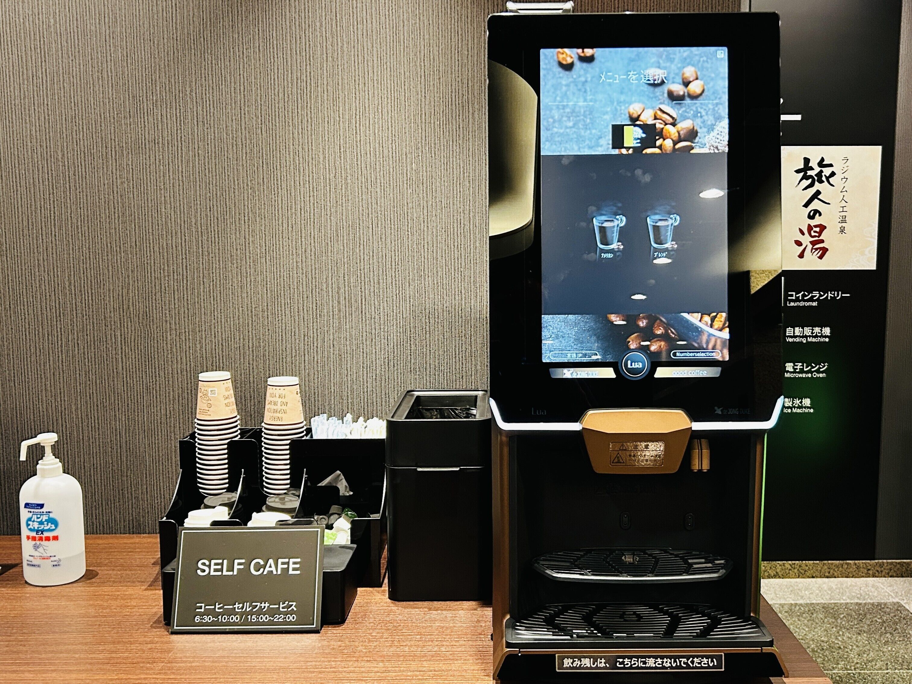 Eine Selbstbedienungskaffee-Station mit digitaler Menüanzeige, Kaffeetassen und einem Automaten.