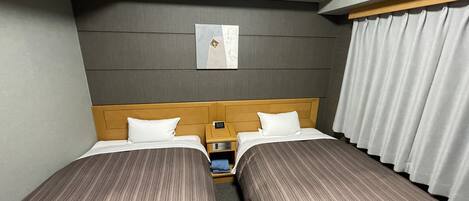 A hotel room with two beds, a nightstand, a wall-mounted clock, and a window with curtains.