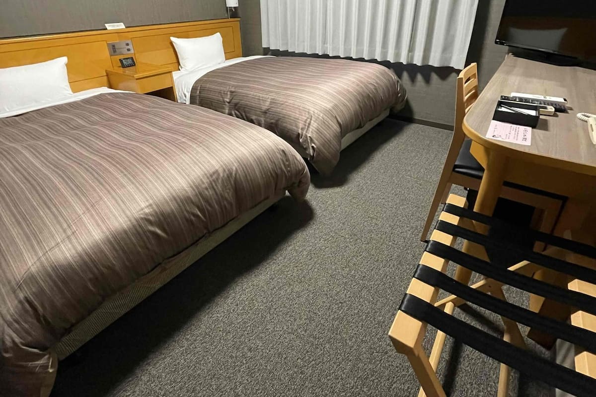 A hotel room with two beds, a desk with a chair, a television, and a window with curtains.