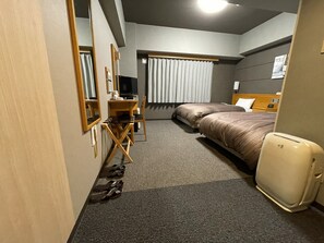 A hotel room with a desk, two beds, a television, and a wardrobe.
