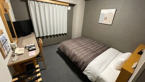 A hotel room with a bed, a desk with a telephone, a chair, a window with curtains, and a wall-mounted picture.
