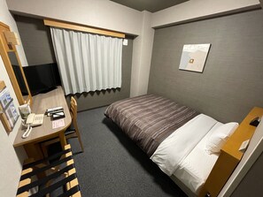Une chambre d’hôtel comprenant un lit, un bureau avec un téléphone, une chaise, une fenêtre avec des rideaux et un tableau accroché au mur.