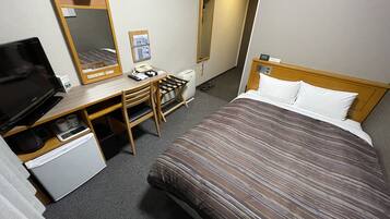 Habitación de hotel con cama, escritorio con computadora, televisor, teléfono y espejo.
