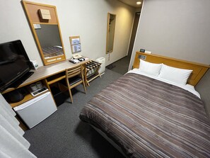 Habitación de hotel con cama, escritorio con computadora, televisor, teléfono y espejo.