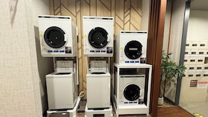 A laundry facility with multiple coin-operated washers and dryers, a step for access, and a potted plant. - Hotel Route-Inn Isahaya Inter (Isahaya)