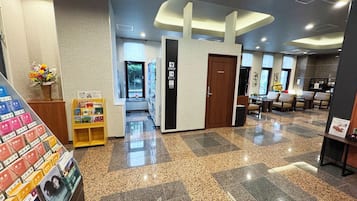 Un vestíbulo de hotel con mostrador de recepción, una puerta que indica 'Sólo personal', una máquina expendedora y un área de descanso con sillas.