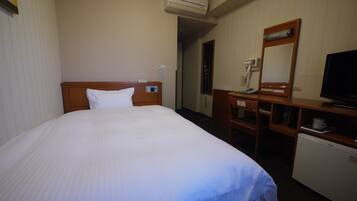 Habitación de hotel con una cama, un escritorio con espejo, televisión y un refrigerador pequeño.