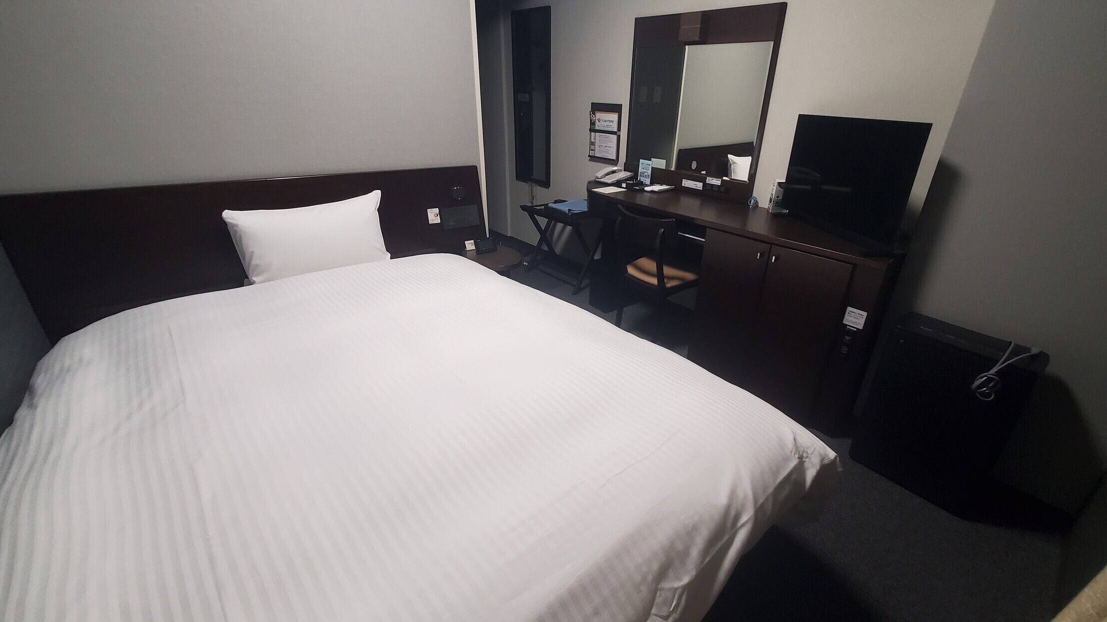Een hotelkamer met een groot bed, een bureau met stoel, een spiegel en een televisie.