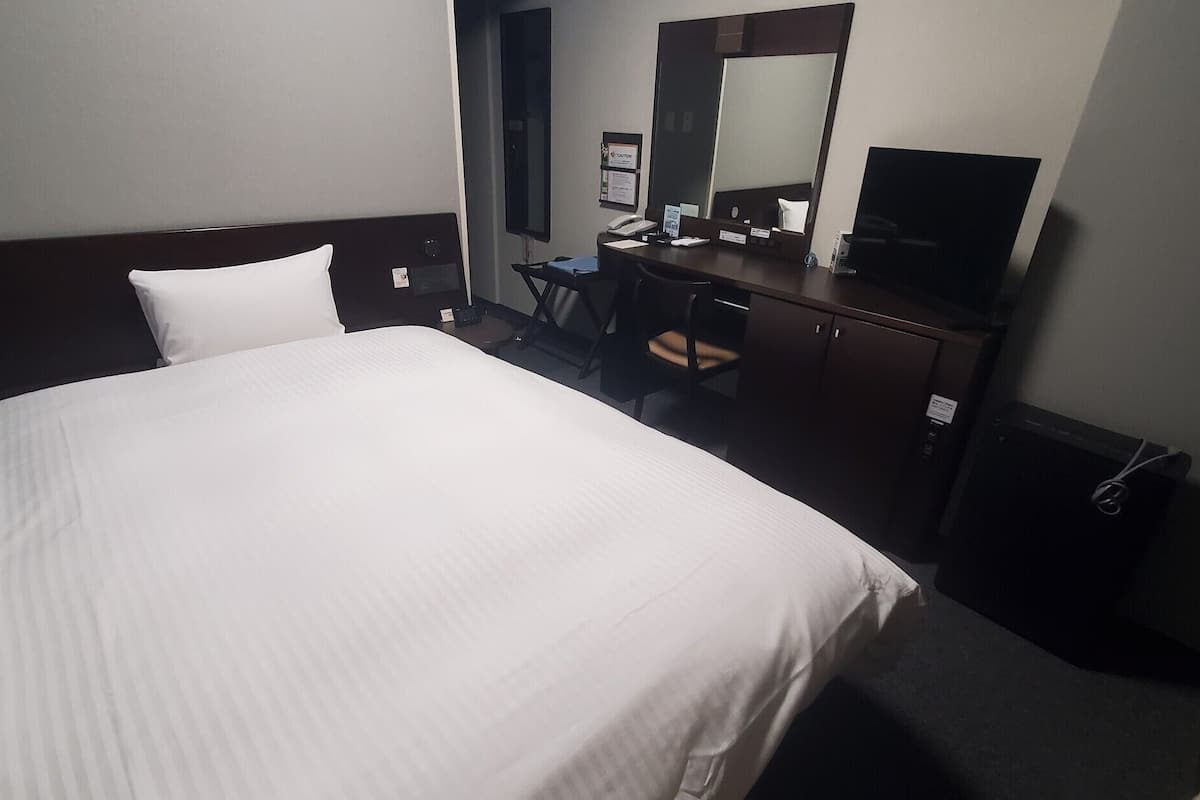 Ein Hotelzimmer mit einem großen Bett, einem Schreibtisch mit Stuhl, einem Spiegel und einem Fernseher.