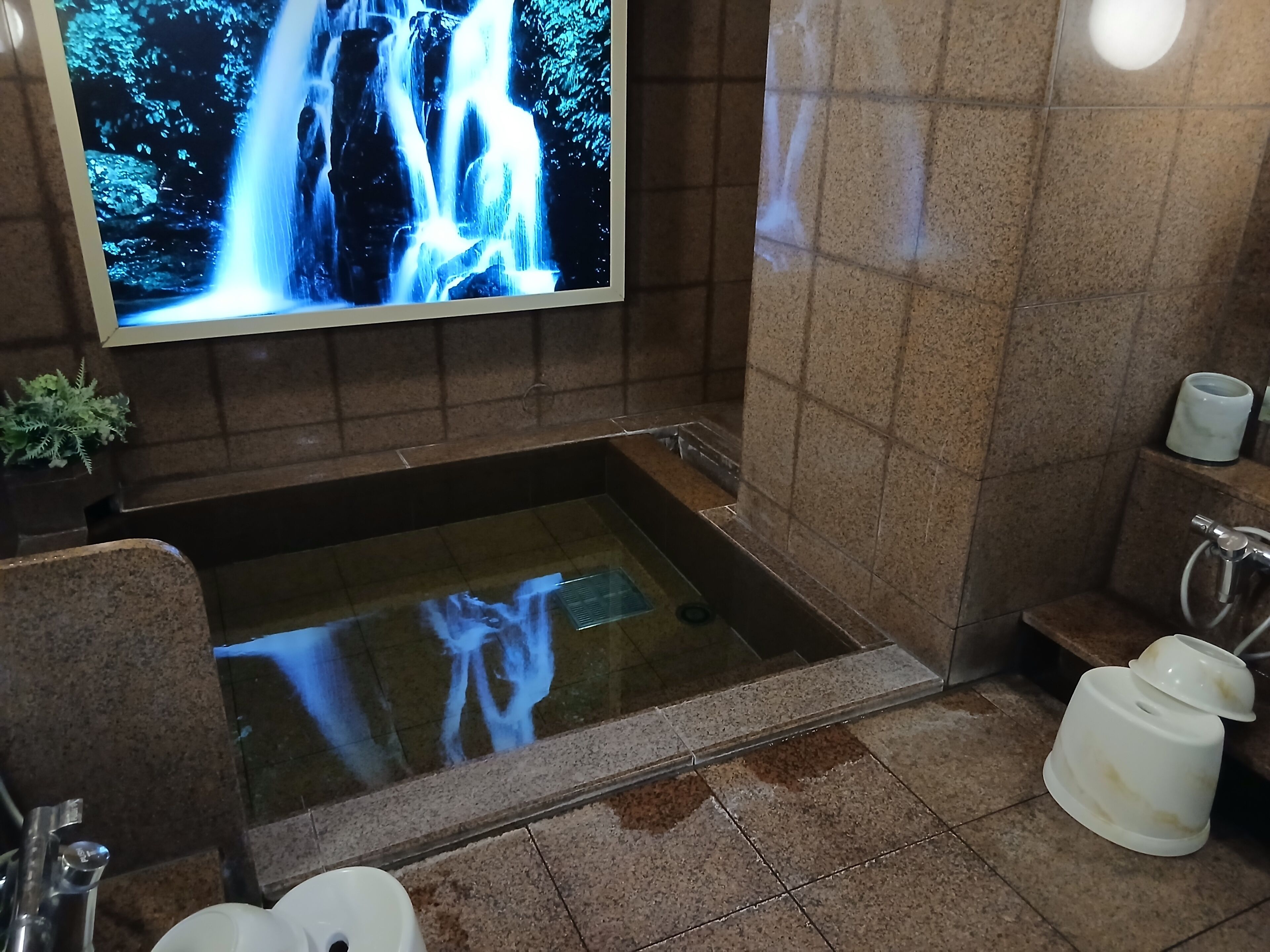 A bathroom with a large screen displaying a waterfall, a bathtub, a toilet, and a sink.