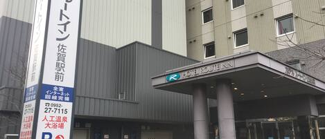 A hotel entrance with a covered area, a vertical sign with Japanese text, and a bench outside.