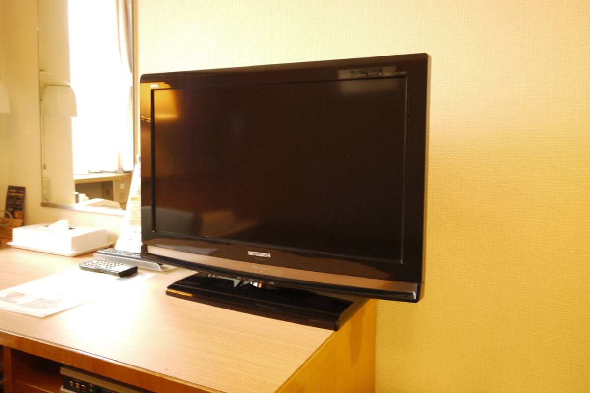 A flat-screen TV on a wooden desk with a remote control and a tissue box.