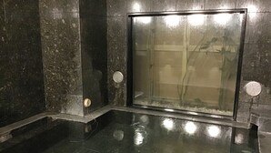 A spa area with a glass-enclosed hot tub, stone walls, and a tiled floor. - Hotel Route Inn Tosu Ekimae (Tosu)