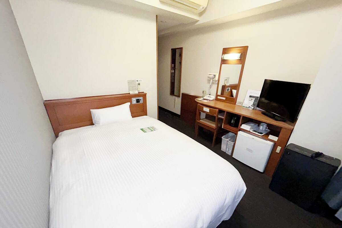 A hotel room with a bed, a desk with a computer, a television, and a small refrigerator.