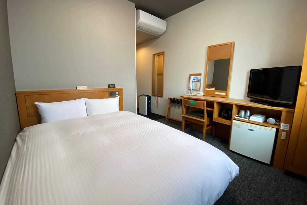 A hotel room with a large bed, a desk with a computer, a television, and a small refrigerator.