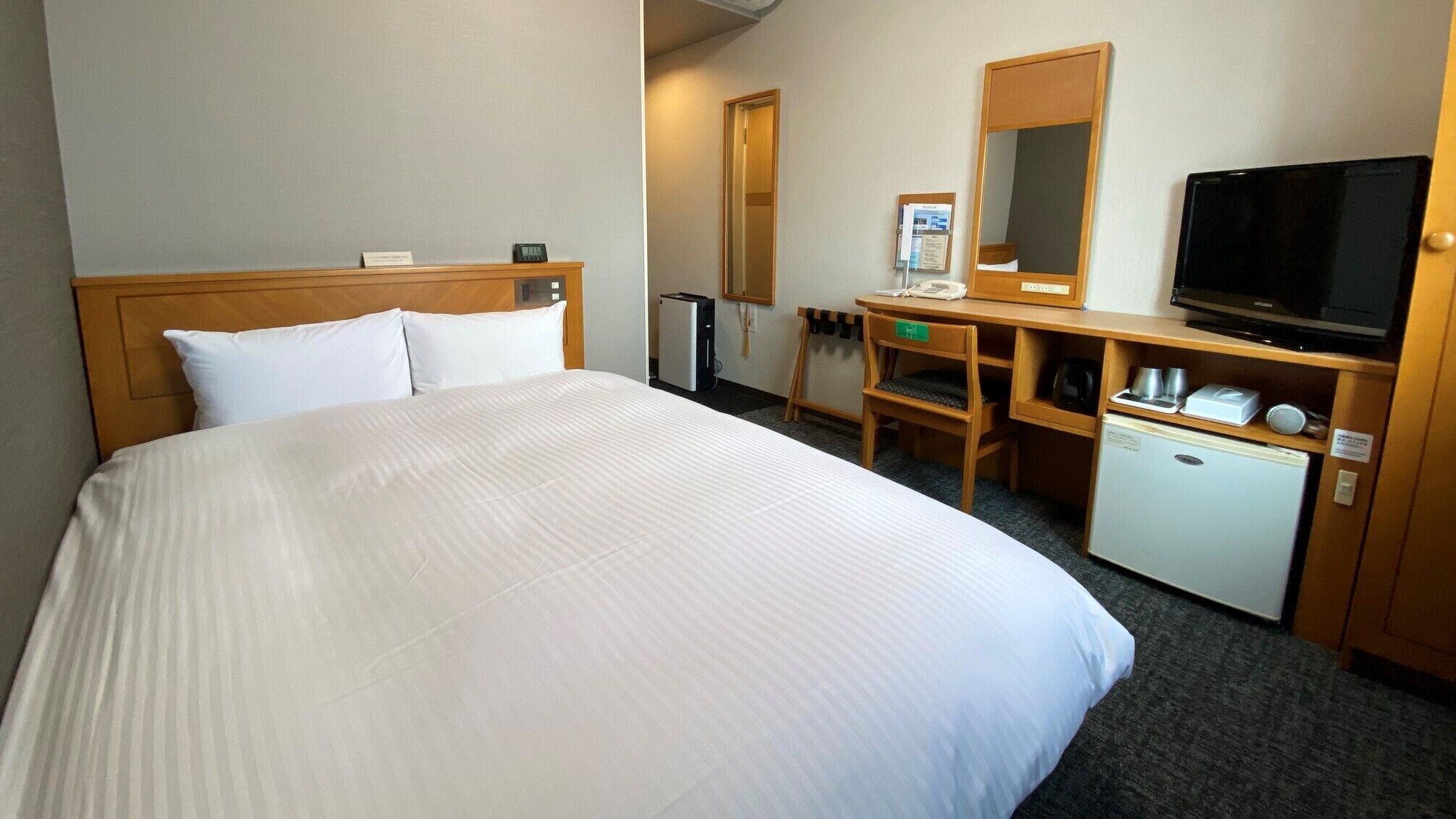 A hotel room with a large bed, a desk with a computer, a television, and a small refrigerator.