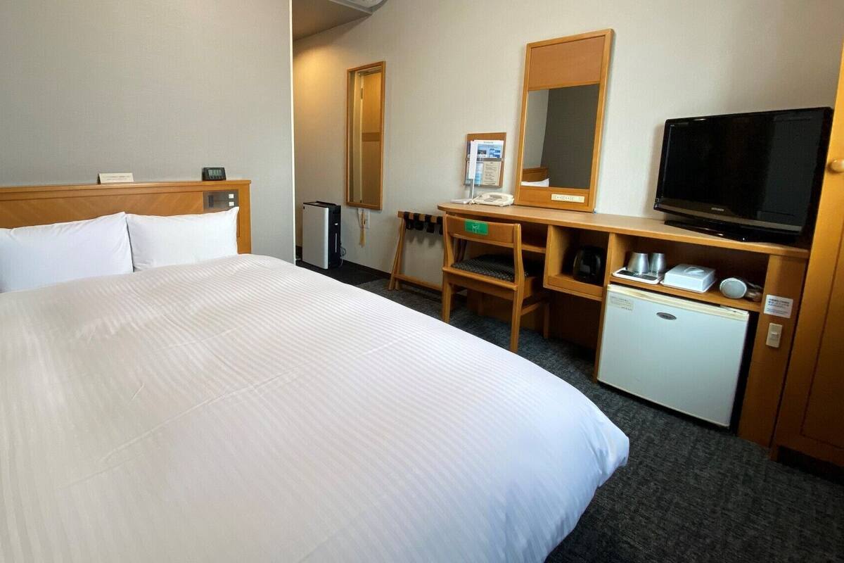 A hotel room with a large bed, a desk with a computer, a television, and a small refrigerator.