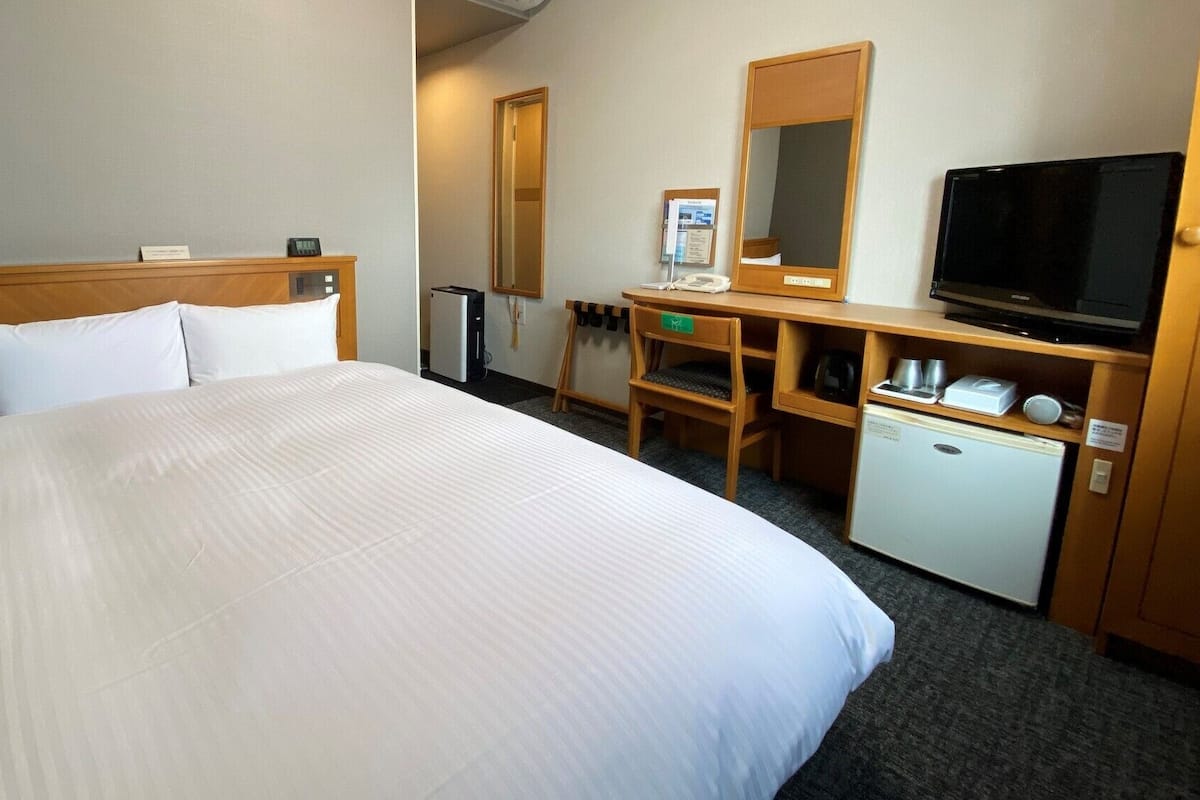 A hotel room with a large bed, a desk with a computer, a television, and a small refrigerator.