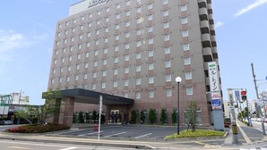 A multi-story hotel with a modern facade, a covered entrance, and a parking area with a traffic cone.