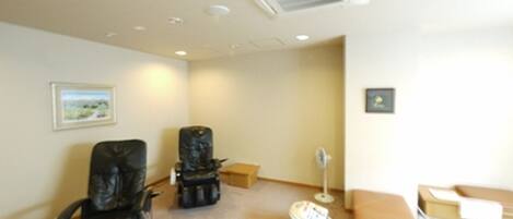 A room with two massage chairs, a small table, a fan, and a picture on the wall.