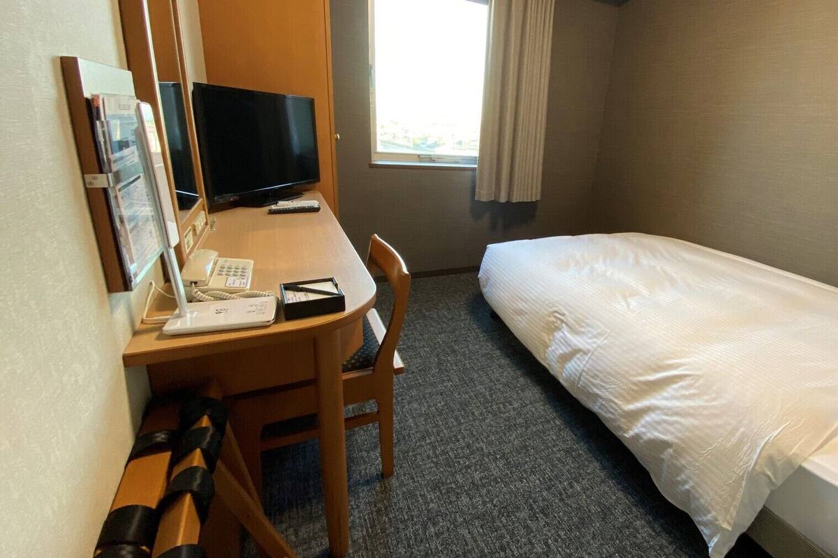 A hotel room with a single bed, a desk with a computer, a telephone, and a chair.
