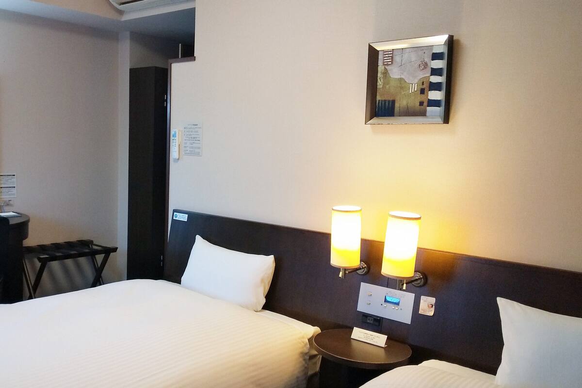 Une chambre d’hôtel avec deux lits, une petite table et des lampes fixées au mur.