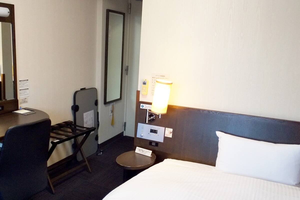 Une chambre d’hôtel comprenant un lit, un bureau, une chaise, une petite table, une lampe et un miroir.